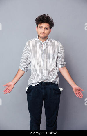 Bel homme haussant et montrant sa poche vide sur fond gris. Looking at camera Banque D'Images