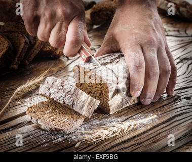 L'homme coupe les mains du pain sur la planche de bois. Banque D'Images