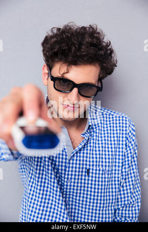 L'Homme à lunettes 3D holding TV remote sur fond gris Banque D'Images