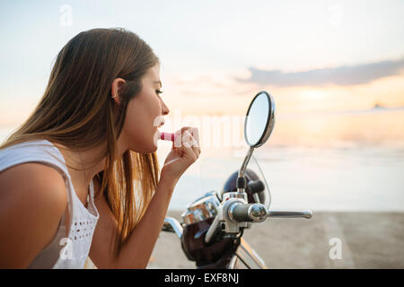 Young woman applying lipstick dans le rétroviseur moto, Manille, Philippines Banque D'Images