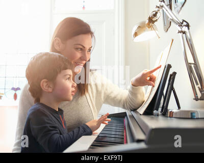 Mère pointant sur partitions d'enseigner aux fils à jouer du piano à la maison Banque D'Images