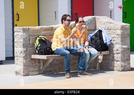 Couple enjoying ice creams assis sur un banc en face de cabanes de plage sur la promenade à Swanage en Juin Banque D'Images