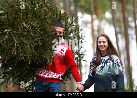 Jeune couple carrying Christmas Tree on shoulders in woods