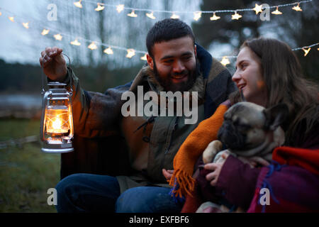 Jeune couple camping avec chien enveloppé dans une couverture Banque D'Images