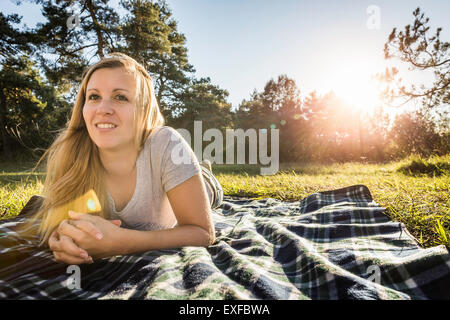 Portrait of young woman lying on picnic blanket in park Banque D'Images