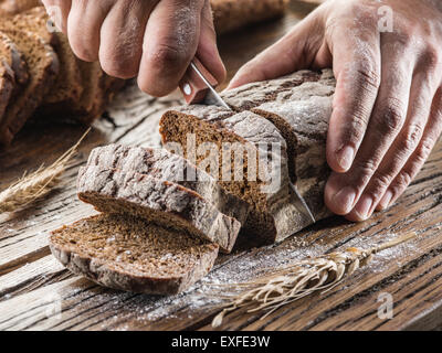 L'homme coupe les mains du pain sur la planche de bois. Banque D'Images