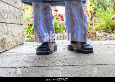 Pieds de l'homme en brun avec chaussons chaussettes bleu, bleu et gris à rayures pyjama robe de chambre dans votre arrière-cour Banque D'Images