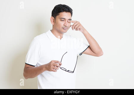 Portrait of Indian guy enlever les lunettes et se frottant les yeux fatigués. Asian man standing sur fond uni avec ombre et co Banque D'Images