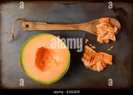 High angle shot d'un cantaloup la moitié à côté d'une cuillère en bois et de la pâte de graines. Vue de dessus en format vertical sur un métal utilisé Banque D'Images