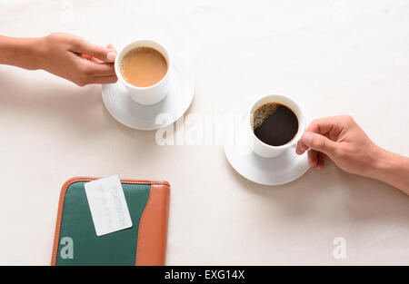 Un homme et une femme ayant atteint pour leurs tasses de café sur une table de café. Passage libre avec seulement des peuples mains affiche actuellement. Banque D'Images