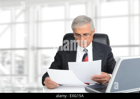 Libre d'un senior businessman looking at documents assis à son bureau à l'intérieur de bureau moderne. Format horizontal avec copie s Banque D'Images