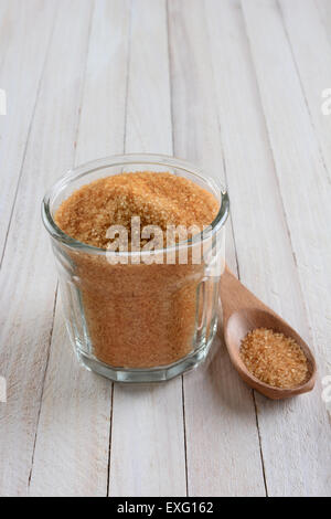 High angle shot d'un bol en verre rempli de sucre brun cristallisé sur une table en bois blanc rustique. Une cuillère de bois est ensuite pose t Banque D'Images