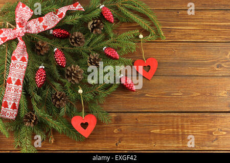 Couronne de Noël - cônes rouges et coeurs en bois rouge sur vert sapin branches sur fond de bois brun Banque D'Images