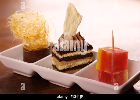 Trois belles de délicieux desserts gourmands sur une plaque blanche. Gâteau de couches de chocolat, caramel, mousse et loukoums. Banque D'Images