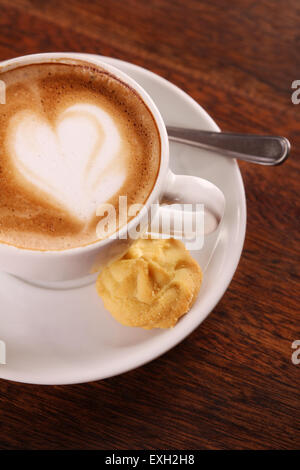 De délicieux cappuccino aromatique dans une tasse de porcelaine blanche avec un biscuit sur le côté sur une table en bois. Banque D'Images