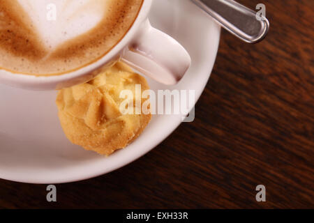 De délicieux cappuccino aromatique dans une tasse de porcelaine blanche avec un biscuit sur le côté sur une table en bois. Image contient l'espace de copie. Banque D'Images