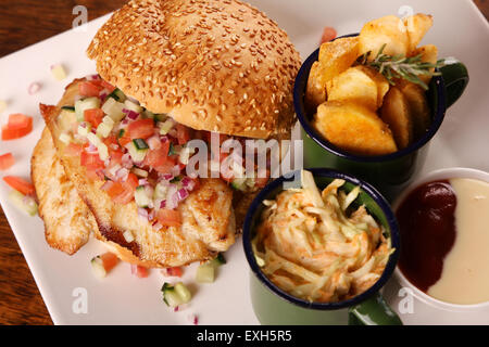 Délicieux burger de poulet avec salade hachée servi avec les quartiers de pommes de terre sur une assiette blanche sur une table en bois. Banque D'Images