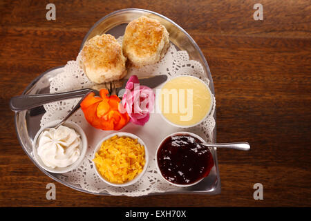 Délicieux scones beurre sur un plateau en forme de coeur argent servi avec du fromage et de la confiture de roses crème conserve sur une table en bois. Droit Banque D'Images