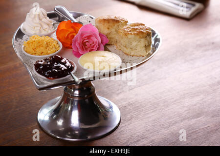 Délicieux scones beurre sur un plateau en forme de coeur argent servi avec du fromage et de la confiture de roses crème conserve sur une table en bois. Banque D'Images