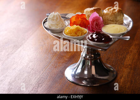 Délicieux scones beurre sur un plateau en forme de coeur argent servi avec du fromage et de la confiture de roses crème conserve sur une table en bois. Banque D'Images