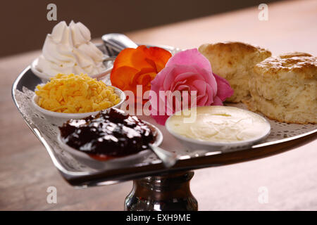 Délicieux scones beurre sur un plateau en forme de coeur argent servi avec du fromage et de la confiture de roses crème conserve sur une table en bois. Banque D'Images