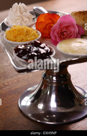 Délicieux scones beurre sur un plateau en forme de coeur argent servi avec du fromage et de la confiture de roses crème conserve sur une table en bois. Banque D'Images