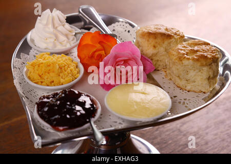 Délicieux scones beurre sur un plateau en forme de coeur argent servi avec du fromage et de la confiture de roses crème conserve sur une table en bois. Banque D'Images