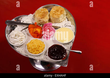 Délicieux scones beurre sur un plateau en forme de coeur argent servi avec du fromage et de la confiture de roses crème conserve sur une table en bois rouge. Banque D'Images