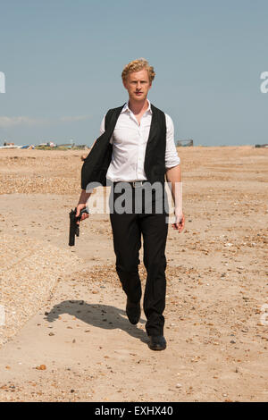 L'homme tenant un pistolet et une longue marche de la plage. Banque D'Images