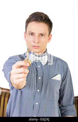 L'homme dans une chemise bleue avec un nœud papillon détient la clé. Modèle masculin montre une clé de la porte de bronze ou cuivre à l'appareil photo. Les jeunes pe Banque D'Images
