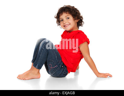 Adorable petit caucasien enfant avec des cheveux bouclés portant un haut à capuchon rouge et bleu jeans. La jeune fille est assise et un sourire Banque D'Images