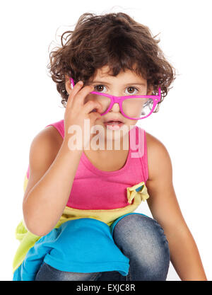 Adorable petit caucasien enfant avec des cheveux bouclés portant une robe rose bleu et jaune. La petite fille joue avec des lunettes funky. Banque D'Images