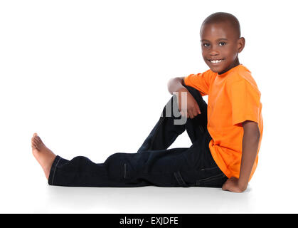 Cute african boy portant un tee-shirt orange et jeans en denim foncé. Le garçon est assis et souriant à la caméra. Banque D'Images