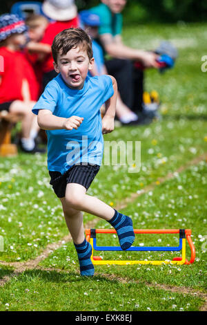 Jeune garçon, 4, sautant par dessus un obstacle dans une école qui s'sports le jour de la race Banque D'Images