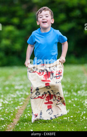 Jeune garçon, 4, en compétition dans la course en sac de sport jour pré-scolaire Banque D'Images