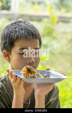 Portrait of Asian Thai pensive boy ressemble à l'os de poisson à tête de serpent, poisson frit mangé sur la plaque clairement Banque D'Images