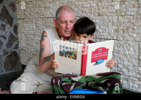 Petit garçon apprendre à lire son anglais Thomas le réservoir du moteur livre à la maison à Java en Indonésie Banque D'Images