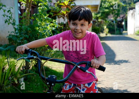 Sept ans petit garçon jouant sur son vélo dans un village-rue à Java en Indonésie Banque D'Images