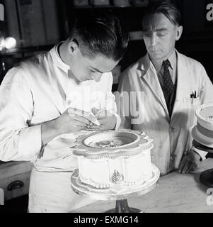 Historique Années 1950 photo montrant un jeune homme l'apprentissage des élèves comment mettre le glaçage sur ou Décorer un gâteau de mariage. Banque D'Images