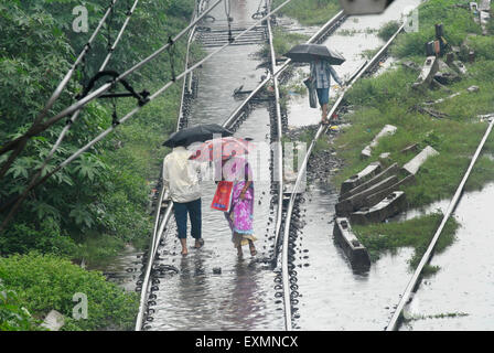 Les navetteurs à pied dans les eaux inondées sur la voie ferrée causée en raison de fortes pluies à la gare Kurla Mumbai Banque D'Images