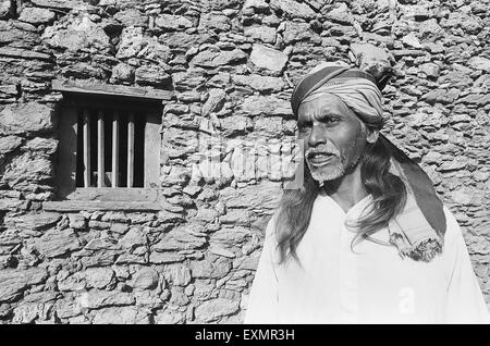 Homme debout rural en dehors de son mur de pierre ; maison ; village Lokur district Dharwar Bijapur district ; ; ; Inde Karnataka Banque D'Images