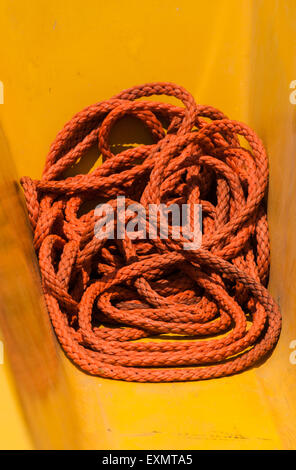 Longue corde orange portant sur le pont de bateau de pêche jaune Banque D'Images