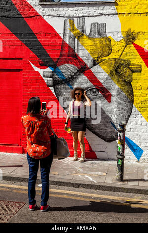 Une jeune femme pose pour une photo en face de certains Graffiti Street Art/off, Brick Lane, Londres, Angleterre Banque D'Images