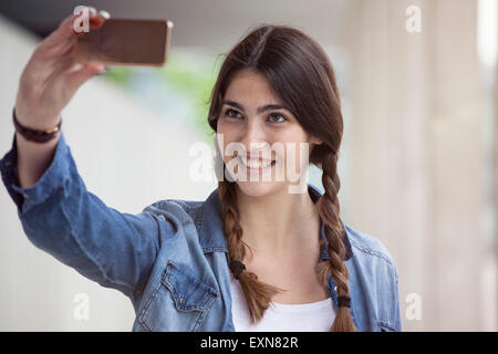 Jeune femme avec des tresses en tenant un smartphone avec selfies Banque D'Images