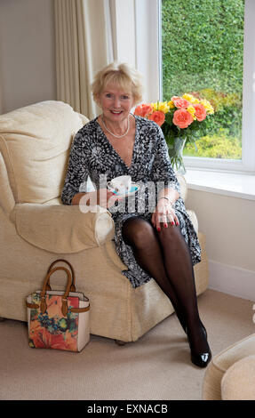 Vieille Femme assise dans un fauteuil confortable ayant une tasse de thé Banque D'Images