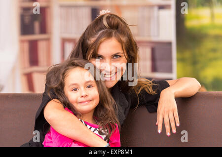 Mère et fille posant joyeusement à l'intérieur en canapé souriant pour appareil photo Banque D'Images