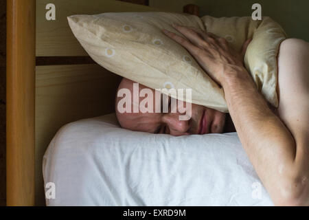 Homme blanc sur le lit avec un oreiller sur la tête dans la journée Banque D'Images