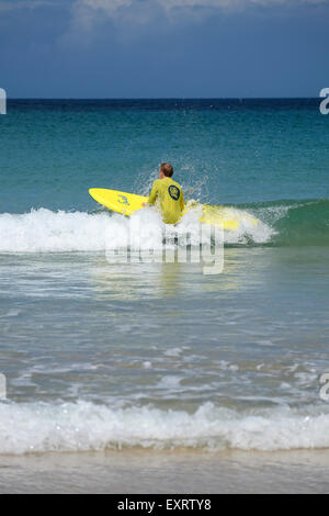 St Ives, Cornwall, UK : l'homme en jaune Surf School T-shirt dans l'eau, apprendre à surfer sur la plage de Porthmeor à St Ives dans Banque D'Images