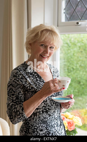 Personnes âgées femme debout par une fenêtre de boire une tasse de thé Banque D'Images