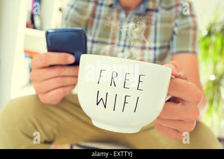 Gros plan du jeune homme de race blanche à l'aide d'un smartphone avec une tasse de café ou de thé avec connexion Wi-Fi gratuite le texte écrit en c Banque D'Images